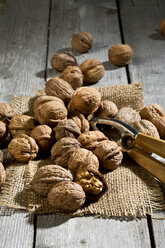 Walnüsse (Juglans regia), Nussknacker und Sackleinen auf Holztisch - MAEF007462