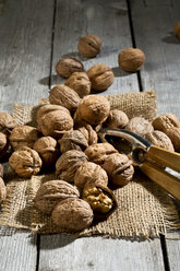Walnuts (Juglans regia), nutcracker and burlap on wooden table - MAEF007462