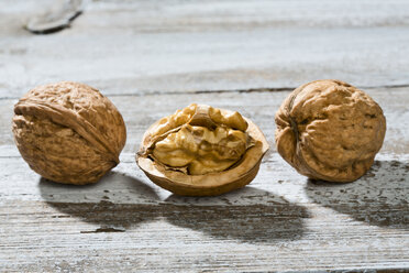 Two whole and a half of a walnut (Juglans regia) on wooden table, close-up - MAEF007465