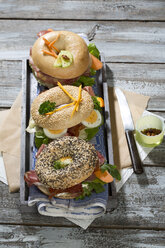 Drei verschiedene Bagels, garniert mit Salami, Wurst, Speckscheiben, Rucola, Kopfsalat, Gurke, Karotte, Ei, Frischkäse und Kresse und Petersilie - MAEF007486