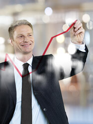 Porträt eines Geschäftsmannes, der eine rote Kurve an einer Glasscheibe zeichnet - STKF000704