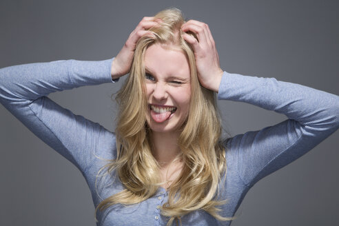 Porträt einer jungen Frau mit herausgestreckter Zunge und Händen auf dem Kopf - MAEF007546