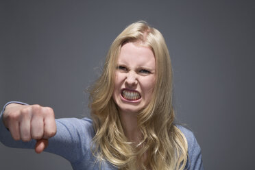 Porträt einer wütenden jungen Frau mit ausgestreckter Faust und gefletschten Zähnen - MAEF007521