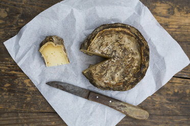 Tomme de Savoie Käse und Messer auf Pergamentpapier auf Holztisch - LVF000352