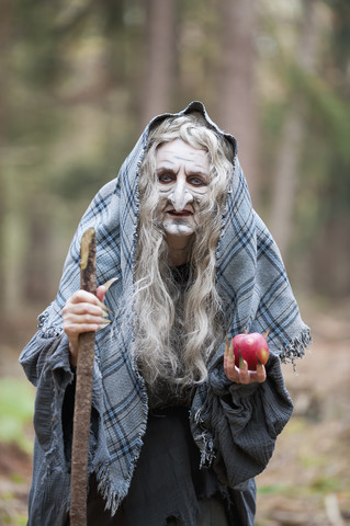 Deutschland, Nordrhein-Westfalen, Mönchengladbach, Szene aus einem Märchen, Hexe hält einen Apfel im Wald, lizenzfreies Stockfoto