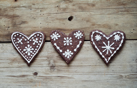 Drei mit Zuckerguss verzierte Lebkuchenherzen auf Holztisch, lizenzfreies Stockfoto