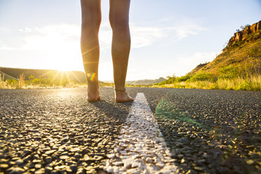 Australia, Western Australia, young woman standing barefoot on empty road - MBEF000947