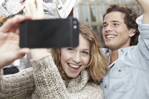 Porträt eines glücklichen jungen Paares, das sich selbst mit einem Smartphone fotografiert, Studioaufnahme - FMKF000930