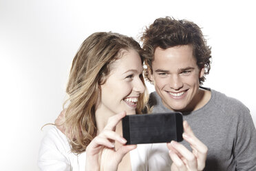 Portrait of happy young couple with smart phone, studio shot - FMKF000950