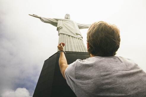 Brasilien, Rio de Janeiro, Corcovado, Mann betet vor der Jesus Christus Erlöser Statue - AMCF000014