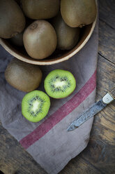 Bowl of kiwis (Actinidia deliciosa) and pocketknife on wooden table - LVF000380