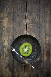 Schale mit einer halben Kiwi (Actinidia deliciosa) und einer Gabel auf einem Holztisch - LVF000378
