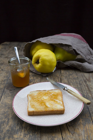 Quitten (Cydonia oblonga), selbstgemachtes Quittengelee und eine Scheibe Toast auf dem Holztisch, lizenzfreies Stockfoto