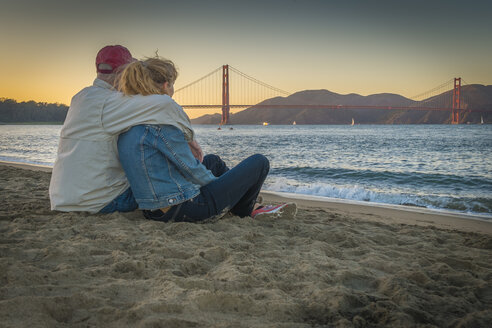 USA, Kalifornien, San Francisco, Älteres Paar sitzt am Strand bei der Golden Gate Bridge in der Dämmerung - ABAF001086