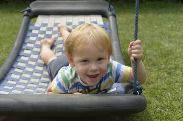 Little boy lying on a swing in the garden - CRF002529