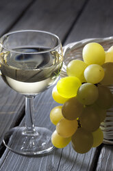 Grüne Weintrauben (Vitis vinifera) in einem weißen Korb und ein Glas Weißwein - CSF020524