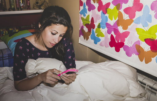 Spanien, Madrid, junge Frau sitzt auf dem Bett und benutzt ein Smartphone - AMCF000030