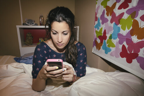 Spanien, Madrid, junge Frau sitzt auf dem Bett und benutzt ein Smartphone - AMCF000031