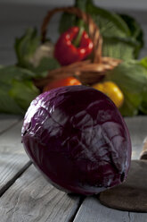 Rotkohl (Brassica oleracea convar. capitata var. rubra) und Korb mit anderem Gemüse im Hintergrund auf grauem Holztisch - CSF020592