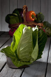 Spitzkohl (Brassica oleracea var. capitata f. alba) und Korb mit anderem Gemüse im Hintergrund auf grauem Holztisch - CSF020587