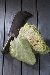 In Scheiben geschnittener Spitzkohl (Brassica oleracea var. capitata für. alba subv. conica) und antikes Hackmesser auf grauem Holztisch - CSF020541