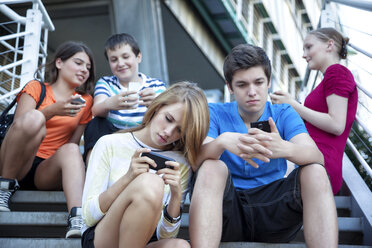 Teenage friends using mobile devices on stairs - MVC000050