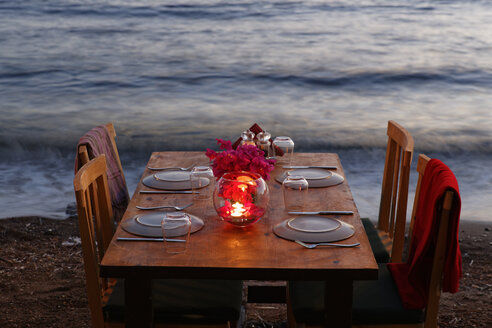 Türkei, Bodrum, Guemuesluek, Gedeckter Tisch am Strand in der Abenddämmerung - SIEF004865