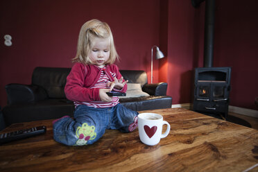 Kleines Mädchen sitzt auf einem Holztisch und testet ein Smartphone - IPF000004