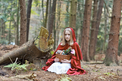 Mädchen als Rotkäppchen verkleidet auf dem Boden sitzend im Wald, lizenzfreies Stockfoto