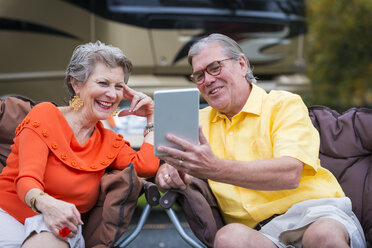 USA, Texas, Senior couple in front of their recreational vehicle using mini tablet pc - ABAF001108