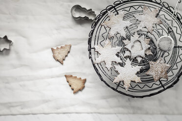 With powdered sugar sprinkled Christmas cookies, cake stand, strainer and cookie cutter on white ground - SBDF000357