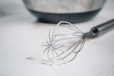 Schneebesen tropft Zuckerguss auf weißen Holztisch - SBDF000370