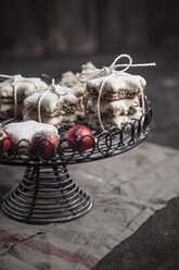 Mit Puderzucker bestreute sternförmige Zimtplätzchen und rote Weihnachtskugeln auf Kuchenständer - SBDF000374