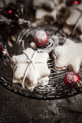 Mit Puderzucker bestreute sternförmige Zimtplätzchen und rote Weihnachtskugeln auf Kuchenständer - SBDF000375