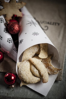 Mandelplätzchen in Papiertüte mit roten Weihnachtskugeln auf Holztisch - SBDF000379