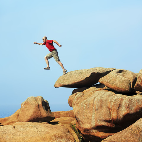 Frankreich, Bretagne, Tregastel, Mann springt auf Felsen, lizenzfreies Stockfoto