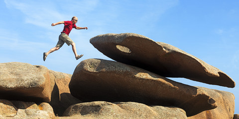 France, Bretagne, Tregastel, Man jumping on rocks stock photo