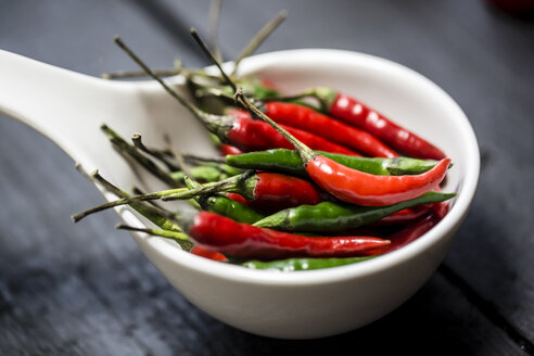 Red and green chilli peppers in a white bowl on wooden table - SARF000175