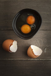 Schale mit zwei aufgeschlagenen Eiern und Eierschalen auf Holztisch, Studioaufnahme - EVGF000311