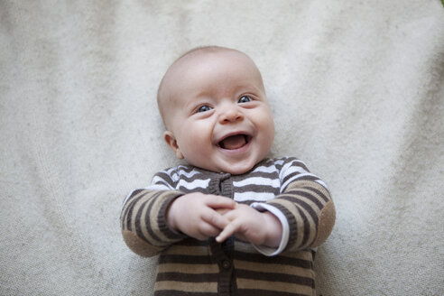 Portrait of laughing baby boy lying on blanket, view from above - RBF001602