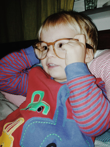 Kleiner Junge mit Schlafanzug und Brille der Mutter, Bonn, NRW, Deutschland, lizenzfreies Stockfoto