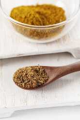 Bowl of curry and wooden spoon with cumin on white wooden board - EVGF000317