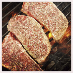 Beef strip loin steaks grilling over hot charcoal fire on barbecue grate - ABAF001147