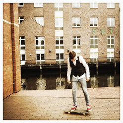 dunkelhaariger europäischer Junge mit Skateboard in der Nähe der Flotte, Deutschland, Hamburg - SEF000300