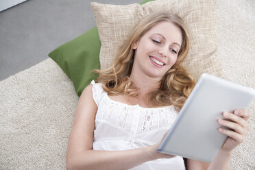 Young woman with tablet computer lying on carpet - PDF000608