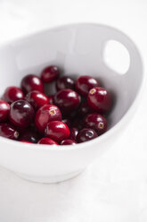 White bowl of fresh cranberries on white table - MYF000095