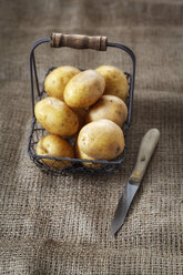 Drahtkorb mit rohen Kartoffeln und Küchenmesser auf Jute - EVGF000327