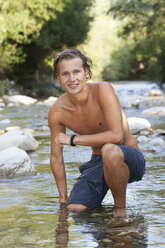 Austria, Salzkammergut, Mondsee, portrait of young man crouching in a brook - WWF003197