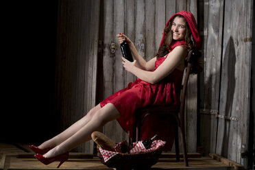 Junge Frau sitzt als Rotkäppchen verkleidet in einer Hütte, Studioaufnahme - MAEF007586
