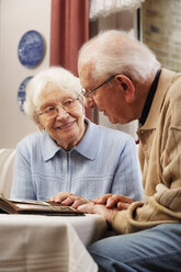 Senior couple watching old photographs at home - BIF000270